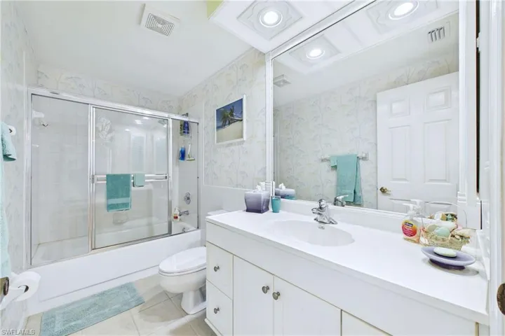 Bathroom featuring vanity, combined bath / shower with glass door, light tile patterned flooring, wallpapered walls, and recessed lighting