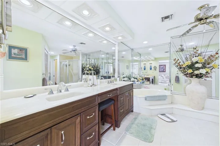 Primary Bathroom with a ceiling fan, a stall shower, double vanity, light tile patterned floors, and a bath