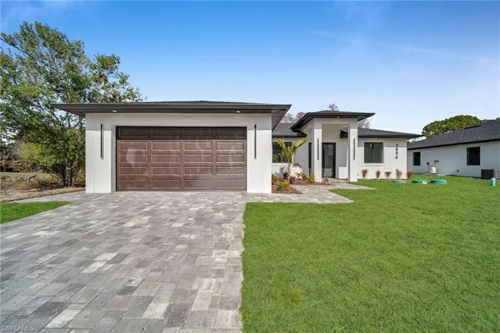 Prairie-style house with a front lawn, decorative driveway, and stucco siding