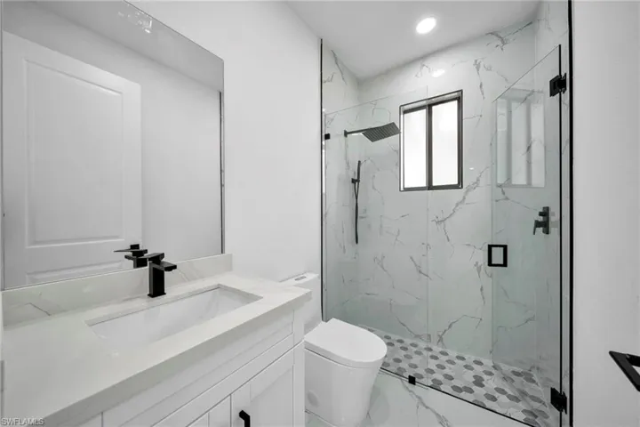 Bathroom featuring vanity, a marble finish shower, light marble finish floors, and recessed lighting
