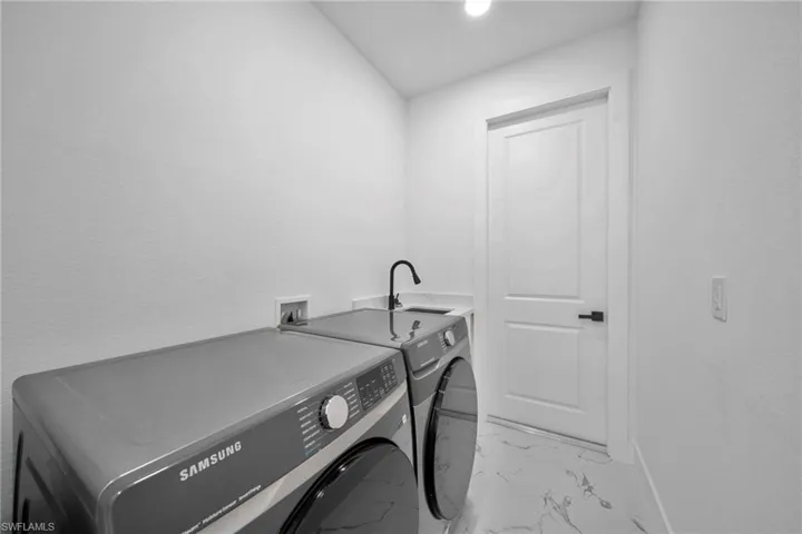 Laundry area featuring washing machine and clothes dryer, light marble finish floors, recessed lighting, and a textured wall