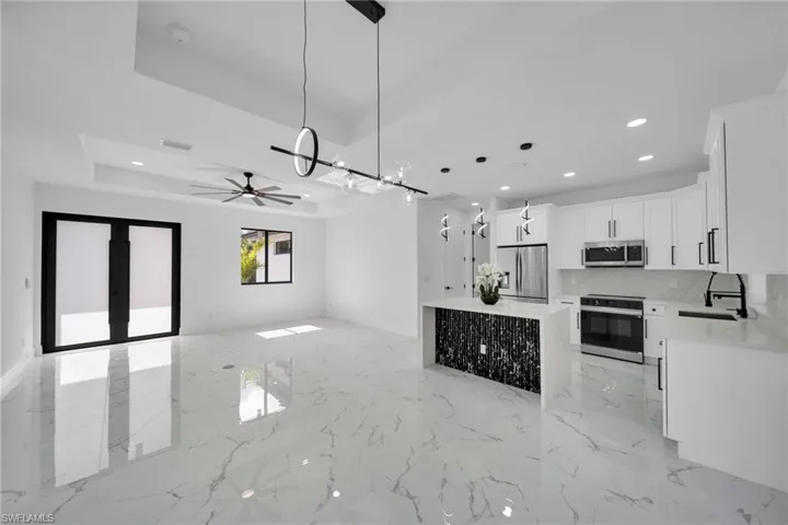 Kitchen with open floor plan, white cabinetry, hanging light fixtures, light stone countertops, and stainless steel appliances