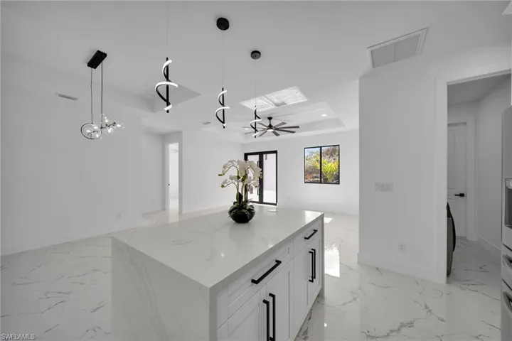 Kitchen with a tray ceiling, decorative light fixtures, open floor plan, a kitchen island, and white cabinetry