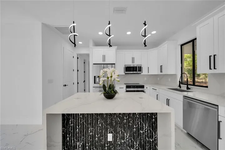 Kitchen with stainless steel appliances, light stone countertops, white cabinetry, and a kitchen island