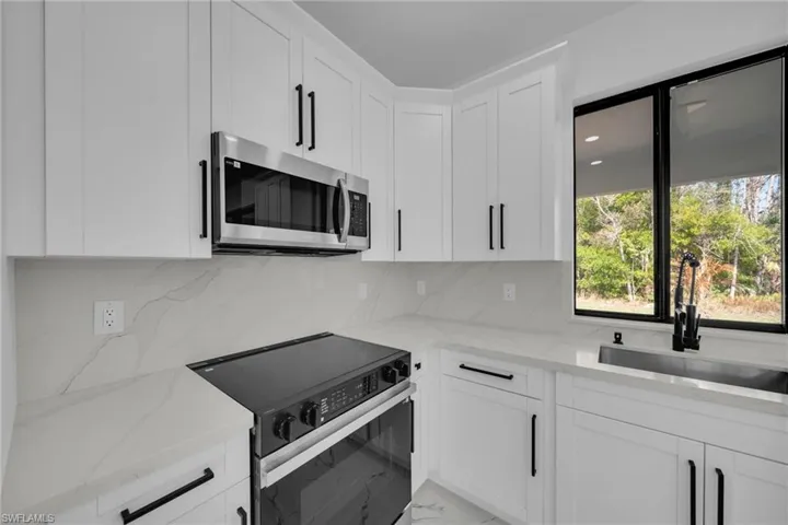 Kitchen featuring black electric range oven, stainless steel microwave, light stone counters, white cabinets, and tasteful backsplash
