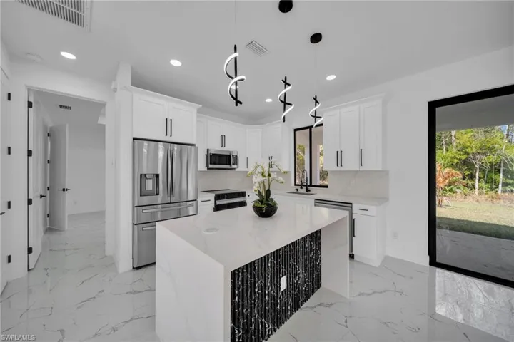 Kitchen featuring stainless steel appliances, a center island, white cabinets, decorative light fixtures, and light stone counters