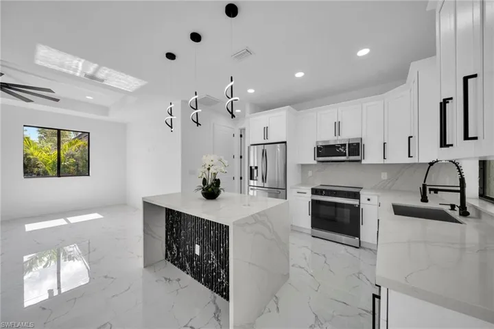 Kitchen featuring stainless steel appliances, light stone counters, decorative light fixtures, white cabinetry, and tasteful backsplash