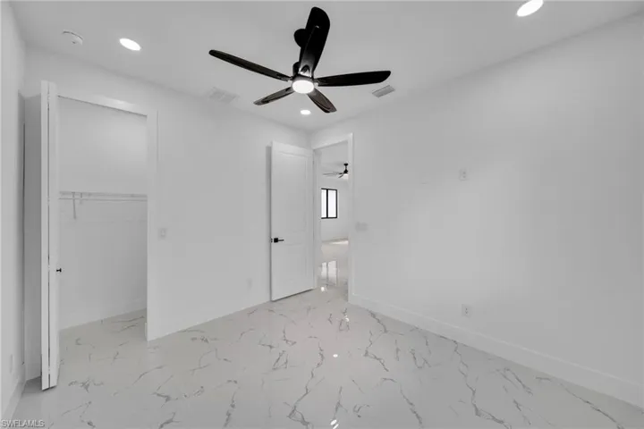 Unfurnished bedroom featuring recessed lighting, light marble finish flooring, a ceiling fan, and a walk in closet