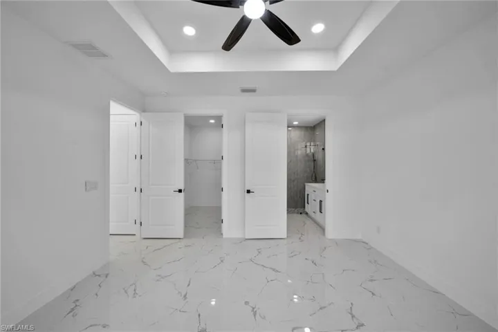 Unfurnished bedroom featuring a walk in closet, a raised ceiling, a ceiling fan, recessed lighting, and ensuite bathroom