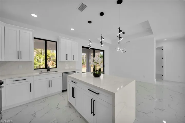Kitchen with a kitchen island, white cabinetry, decorative light fixtures, light stone countertops, and dishwasher