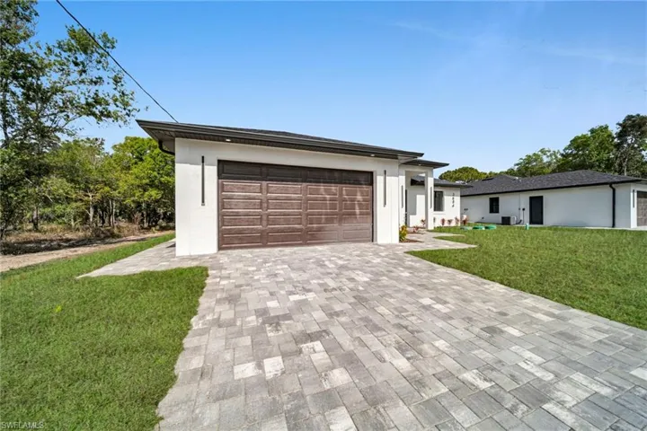 Prairie-style home with a front lawn, decorative driveway, a garage, and stucco siding