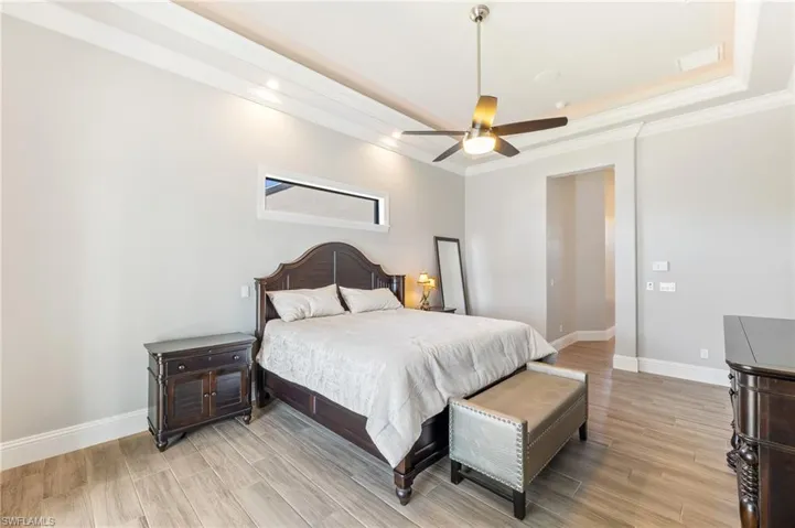 Bedroom featuring light wood-type flooring, ornamental molding, a raised ceiling, ceiling fan, and recessed lighting