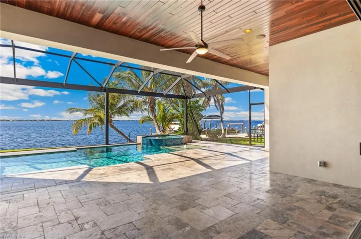 View of swimming pool with a patio area, ceiling fan, a water view, and glass enclosure