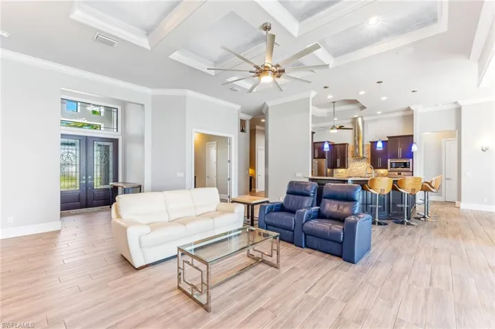 Living room featuring a ceiling fan, coffered ceiling, crown molding, light wood finished floors, and french doors