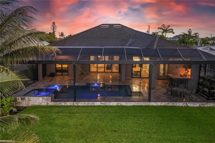 Rear view of property featuring a lawn, a pool with connected hot tub, a patio area, and glass enclosure
