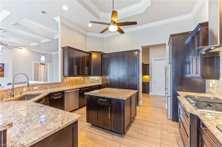 Kitchen featuring stainless steel appliances, wall chimney range hood, a ceiling fan, light stone counters, and hanging light fixtures