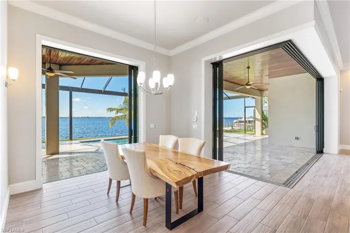 Dining area featuring light wood-style flooring, a water view, a chandelier, ornamental molding, and a ceiling fan