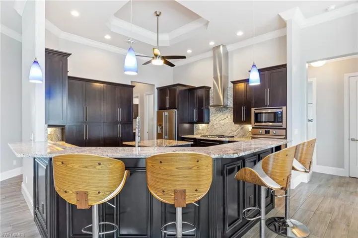 Kitchen with stainless steel appliances, wall chimney exhaust hood, a breakfast bar, a peninsula, and tasteful backsplash
