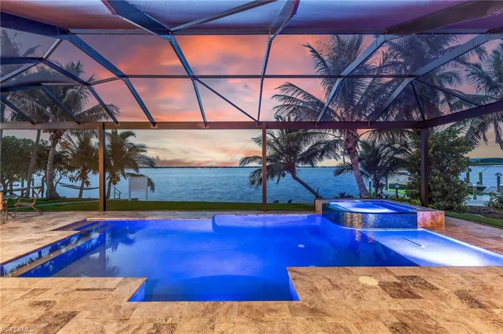 Pool at dusk featuring a water view, a patio area, a lanai, and a pool with connected hot tub