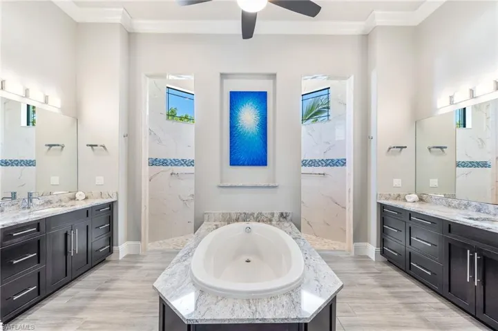 Full bath featuring a bath, a marble finish shower, ceiling fan, two vanities, and ornamental molding