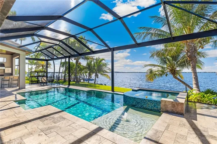 View of pool featuring a patio area, a water view, glass enclosure, and a pool with connected hot tub