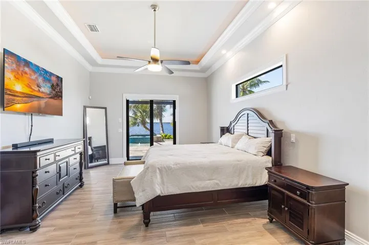 Bedroom with access to exterior, a raised ceiling, light wood-type flooring, ornamental molding, and a ceiling fan