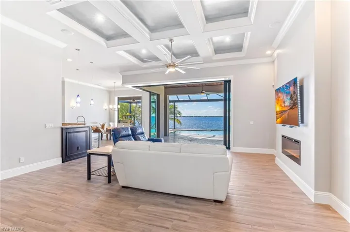 Living area featuring crown molding, light wood-style floors, a glass covered fireplace, a ceiling fan, and coffered ceiling