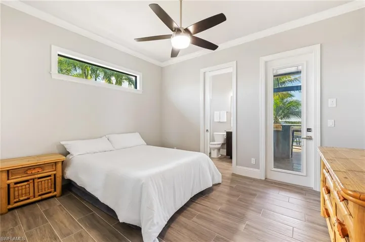 Bedroom with multiple windows, dark wood finished floors, crown molding, and connected bathroom