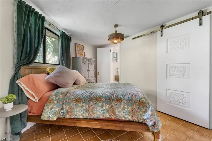 Tiled bedroom featuring a textured ceiling, a barn door, and ceiling fan