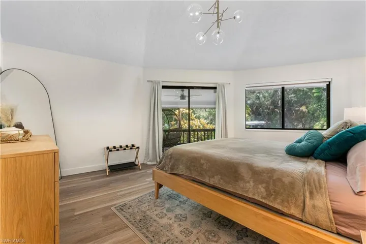 Bedroom with vaulted ceiling, wood-type flooring, access to exterior, and a notable chandelier