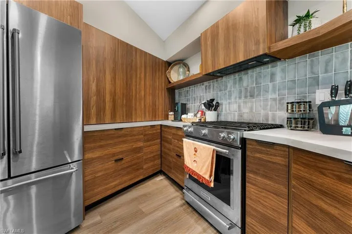 Kitchen featuring ventilation hood, high end appliances, light hardwood / wood-style floors, lofted ceiling, and decorative backsplash