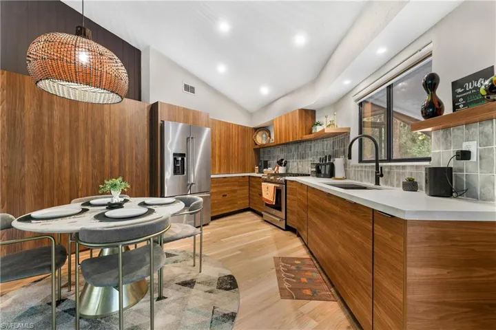 Kitchen with stainless steel appliances, sink, decorative backsplash, lofted ceiling, and light hardwood / wood-style floors