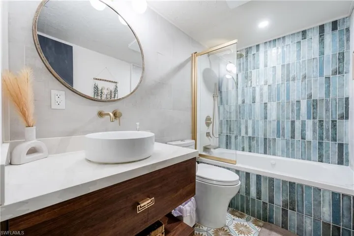 Full bathroom featuring vanity, toilet, tile walls, and combined bath / shower with glass door