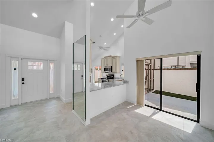 Kitchen with high vaulted ceiling, stainless steel appliances, light stone counters, ceiling fan, and cream cabinets