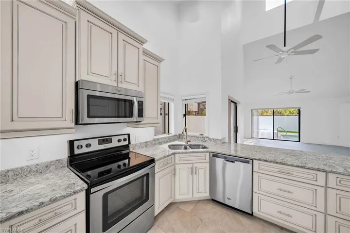 Kitchen with light stone countertops, stainless steel appliances, ceiling fan, sink, and high vaulted ceiling