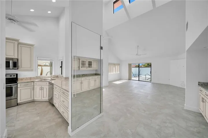 Kitchen featuring high vaulted ceiling, ceiling fan, cream cabinets, and appliances with stainless steel finishes