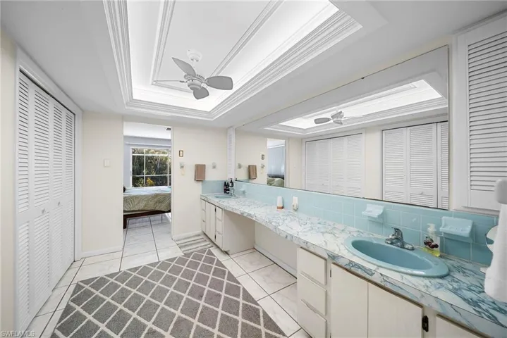 Ensuite bathroom featuring a closet, double vanity, a ceiling fan, and a tray ceiling