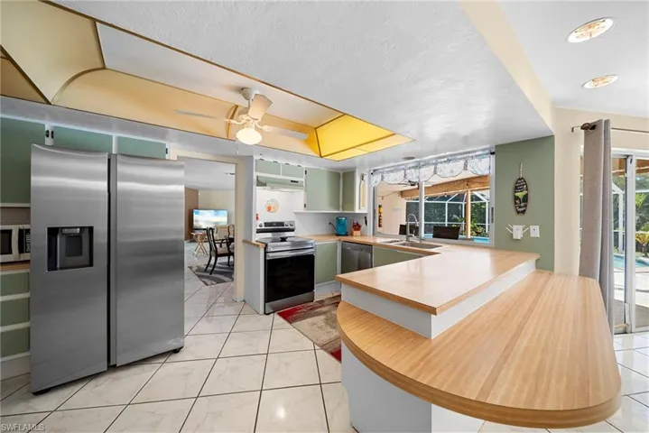 Kitchen featuring appliances with stainless steel finishes, green cabinets, peninsula, and ceiling fan. Views and serving access to pool