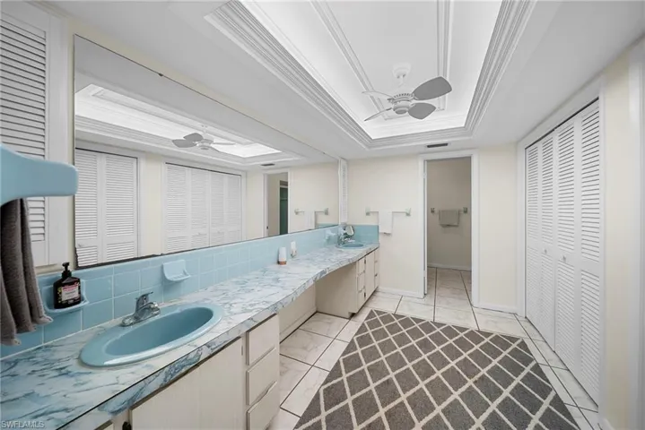 Ensuite bathroom with a closet, ceiling fan, double vanity, a raised ceiling, and ornamental molding