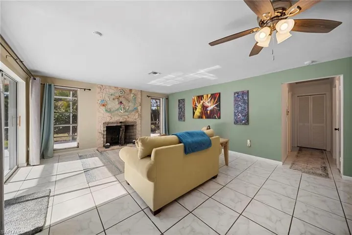 Living area with a stone fireplace, tile floor, large sliding doors and windows providing a healthy amount of natural light, and ceiling fan