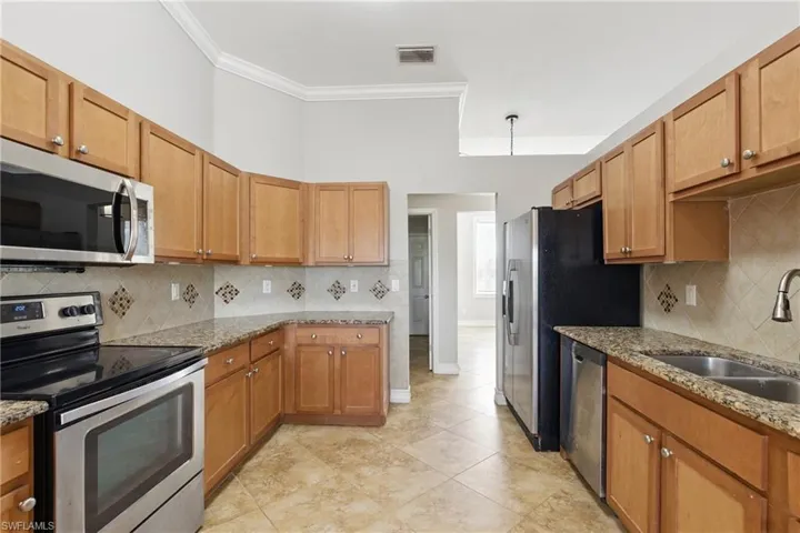 Kitchen with crown molding, appliances with stainless steel finishes, light stone counters, a sink, and visible vents