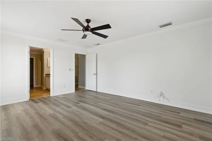 Unfurnished bedroom featuring visible vents, ornamental molding, wood finished floors, baseboards, and ensuite bathroom