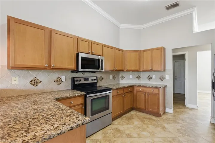 Kitchen featuring appliances with stainless steel finishes, light stone counters, decorative backsplash, visible vents, and ornamental molding
