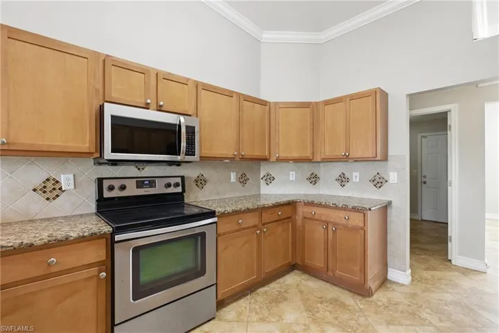 Kitchen featuring ornamental molding, decorative backsplash, appliances with stainless steel finishes, and light stone countertops