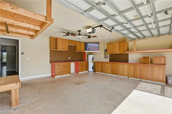 Garage featuring baseboards, a garage door opener, water heater, and electric panel