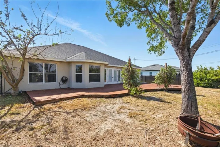 Back of property featuring french doors, a lawn, a deck, a shingled roof, and stucco siding