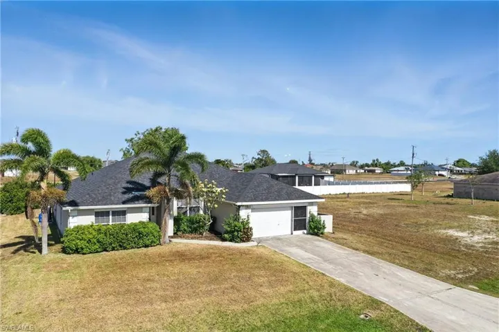 View of front of home with driveway, roof with shingles, a front yard, a garage, and fence