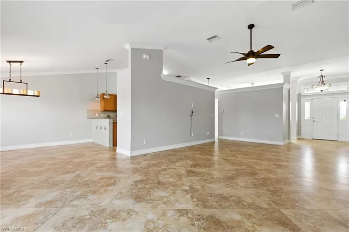 Unfurnished living room featuring visible vents, ornamental molding, baseboards, and a ceiling fan