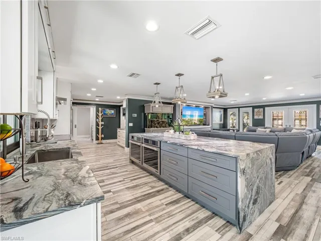 Two tone kitchen with light stone counters, open floor plan, decorative light fixtures, a center island, and two tone color scheme