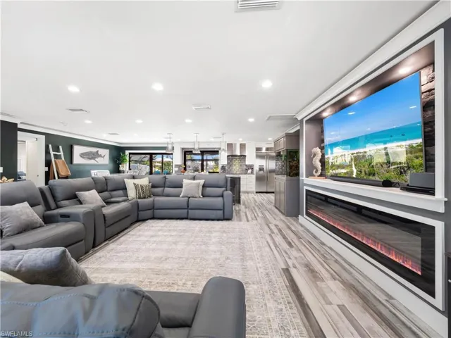 Living area with recessed lighting, ornamental molding, light wood finished floors, and a glass covered fireplace